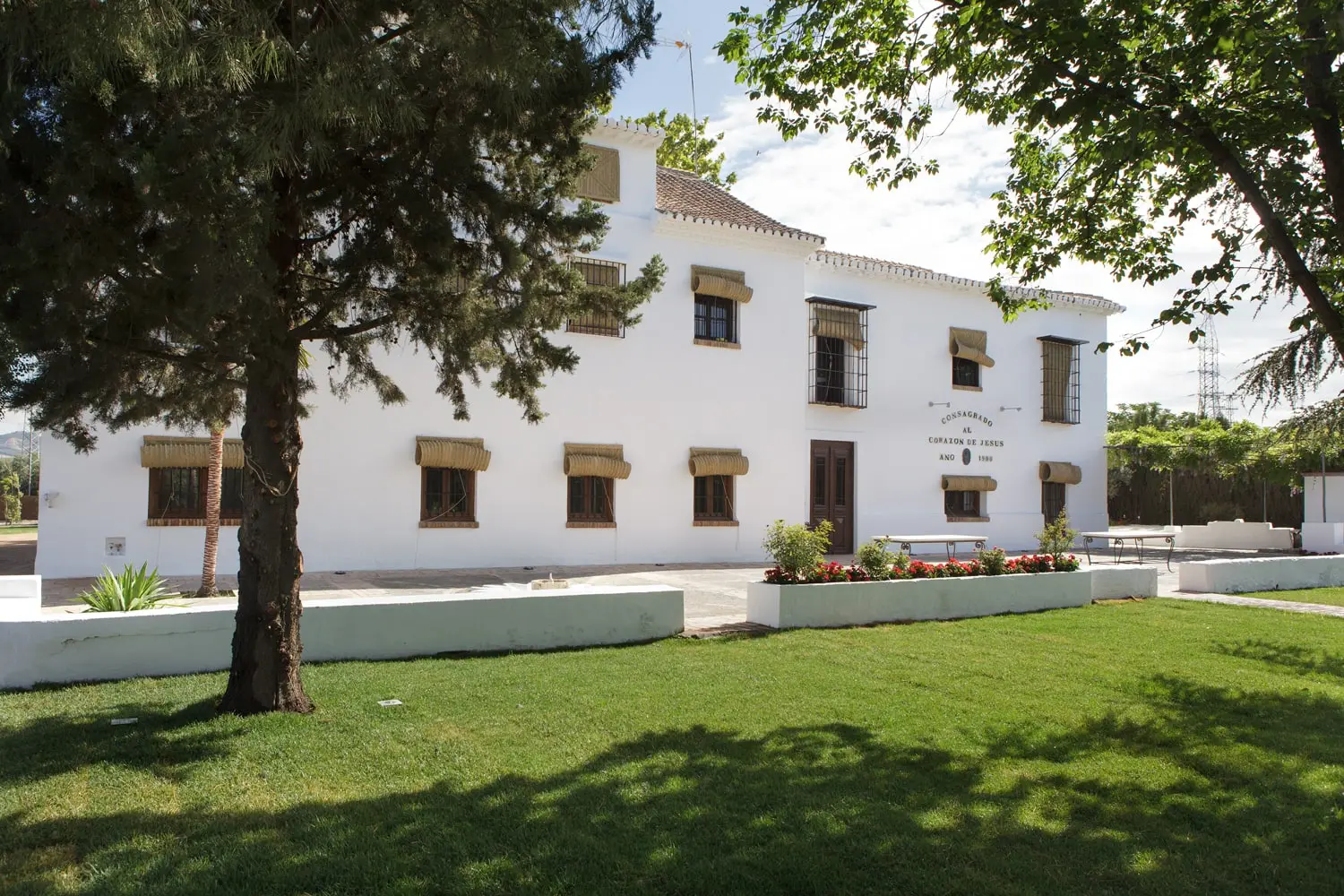 Fachada principal del cortijo sobre el césped, con la placa «Consagrado al Corazón de Jesús, año 1900»